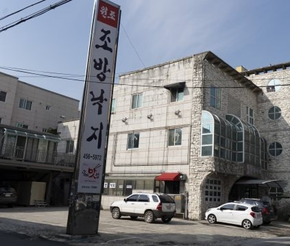 3층 석조 건물과 세로 기둥 간판 «원조 조방낙지 456-5972», 앞 주차장의 차들