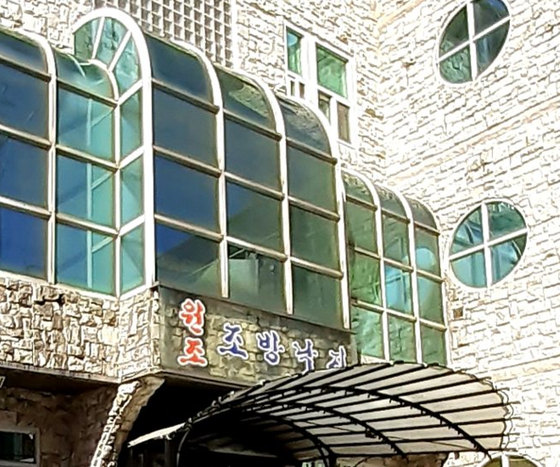 맑은 날 석조 건물 정면 — 아치형 유리창, 입구 위 «원조 조방낙지» 글자 간판과 곡선 차양