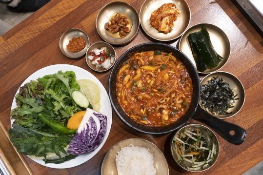 위에서 본 상차림 — 가운데 낙지볶음 팬, 왼쪽 쌈 채소 접시, 둘레 놋그릇 반찬과 김가루·냉국, 아래 놋그릇 밥