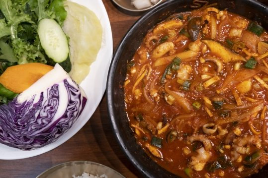 팬 가득한 낙지볶음과 왼쪽 쌈 채소 접시(상추·오이·양배추·당근·적양배추)